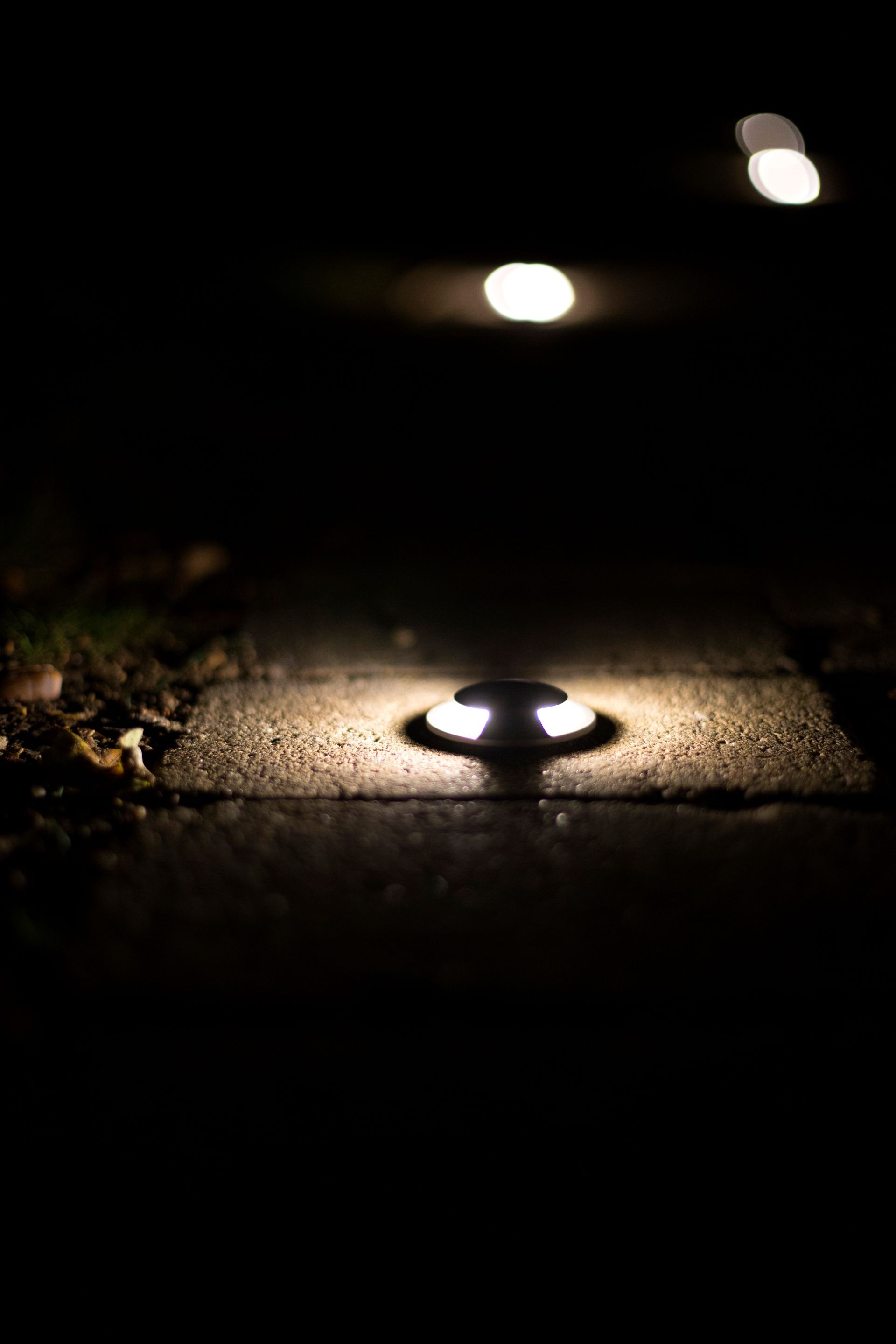 Ground-level walkway lights illuminate a dark pathway at night, with two others in the distance.