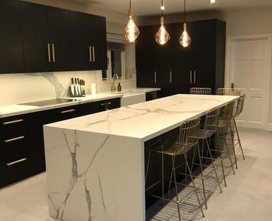 Modern kitchen with black cabinets, white marble countertops, and gold accents.
