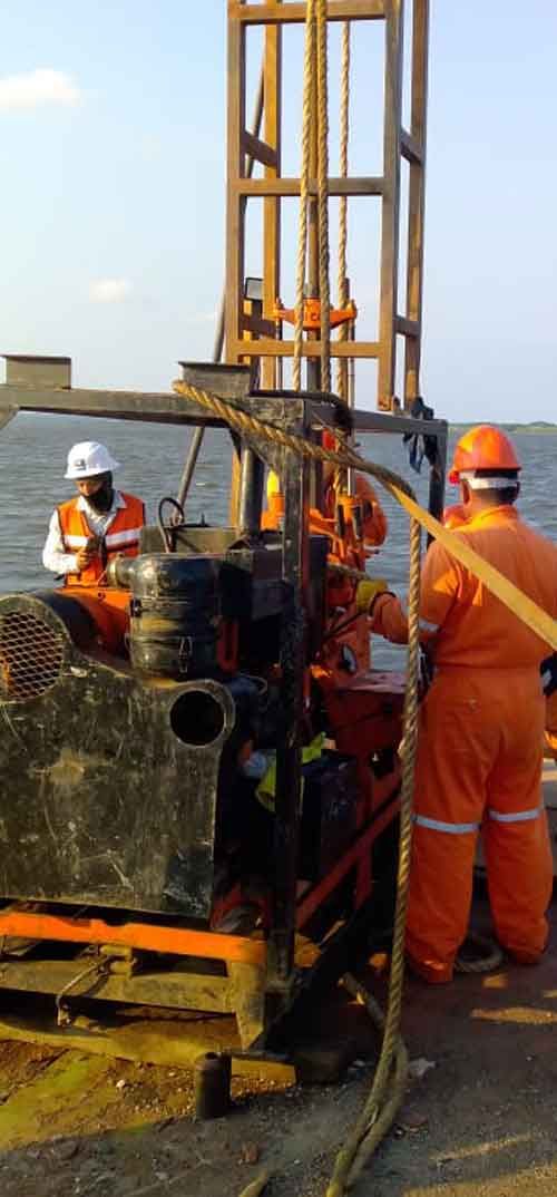 Los trabajadores con monos de color naranja operan maquinaria en un sitio de perforación, con una plataforma al fondo.