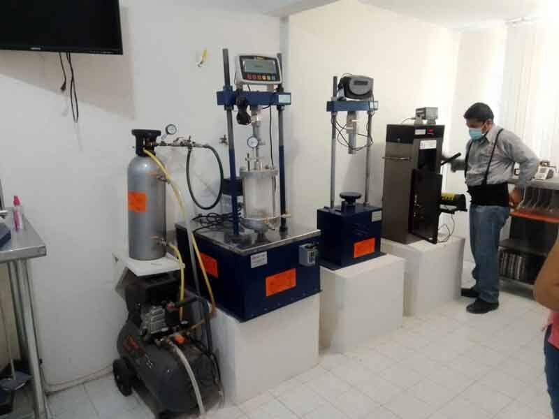 Un hombre con bata de laboratorio opera un equipo de análisis de suelos. Tanque de aire comprimido, maquinaria y sala blanca.