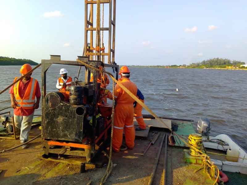 Los trabajadores con overoles de color naranja operan equipos de perforación en una barcaza en un cuerpo de agua.