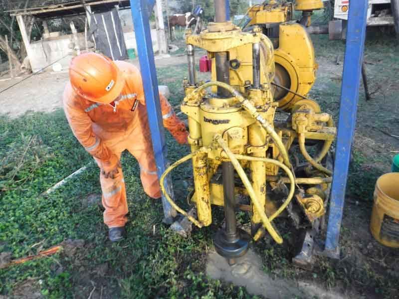 Una persona con un mono naranja opera una máquina perforadora amarilla al aire libre.