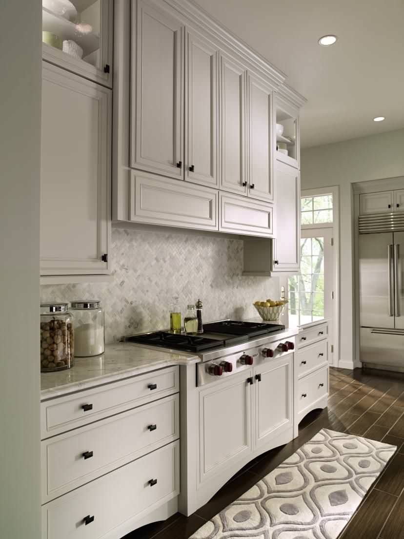 A kitchen with white cabinets , a stove , a sink , and a rug.