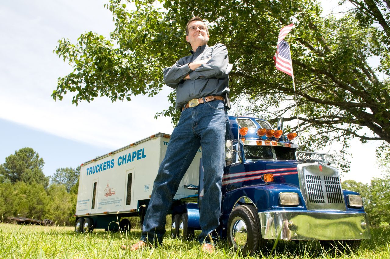 Man standing with arms crossed next to a miniature blue and silver truck with 