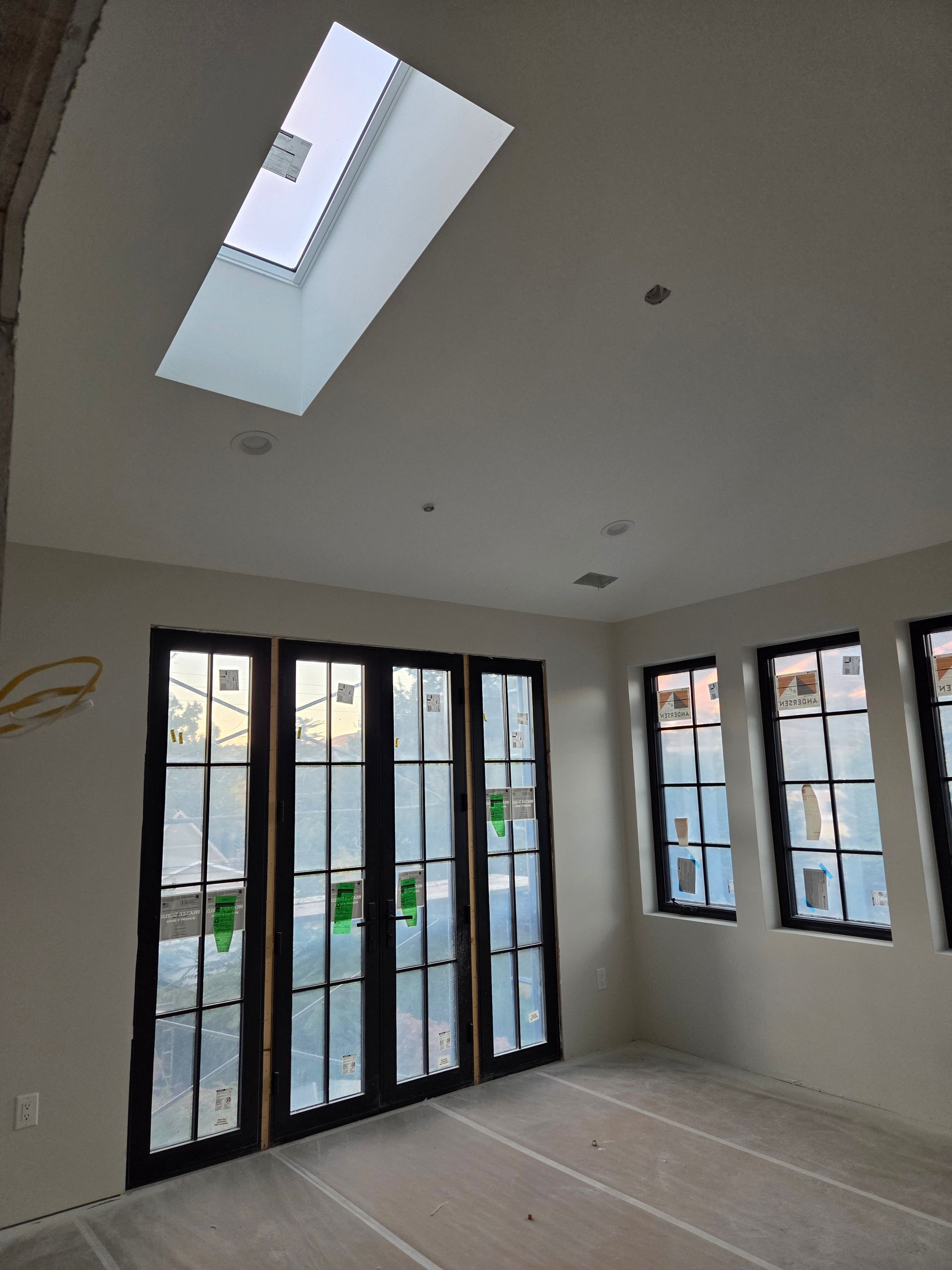 Room interior with skylight and dark-framed doors/windows. White walls and ceiling, unfinished floor.