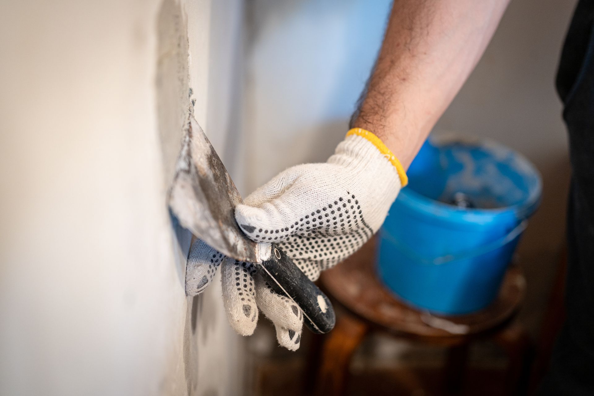 A gloved hand using a small putty knife to press thick patching compound into a drywall hole