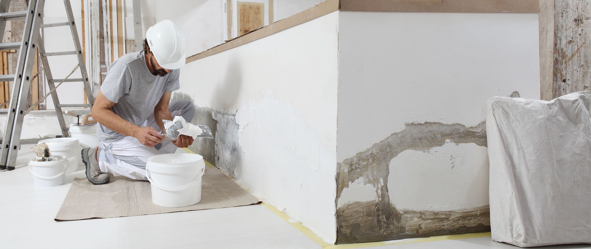 Drywall repair contractor applying joint compound to a wall in a residential home. Drywall repair contractor applying joint compound to a wall in a residential home.