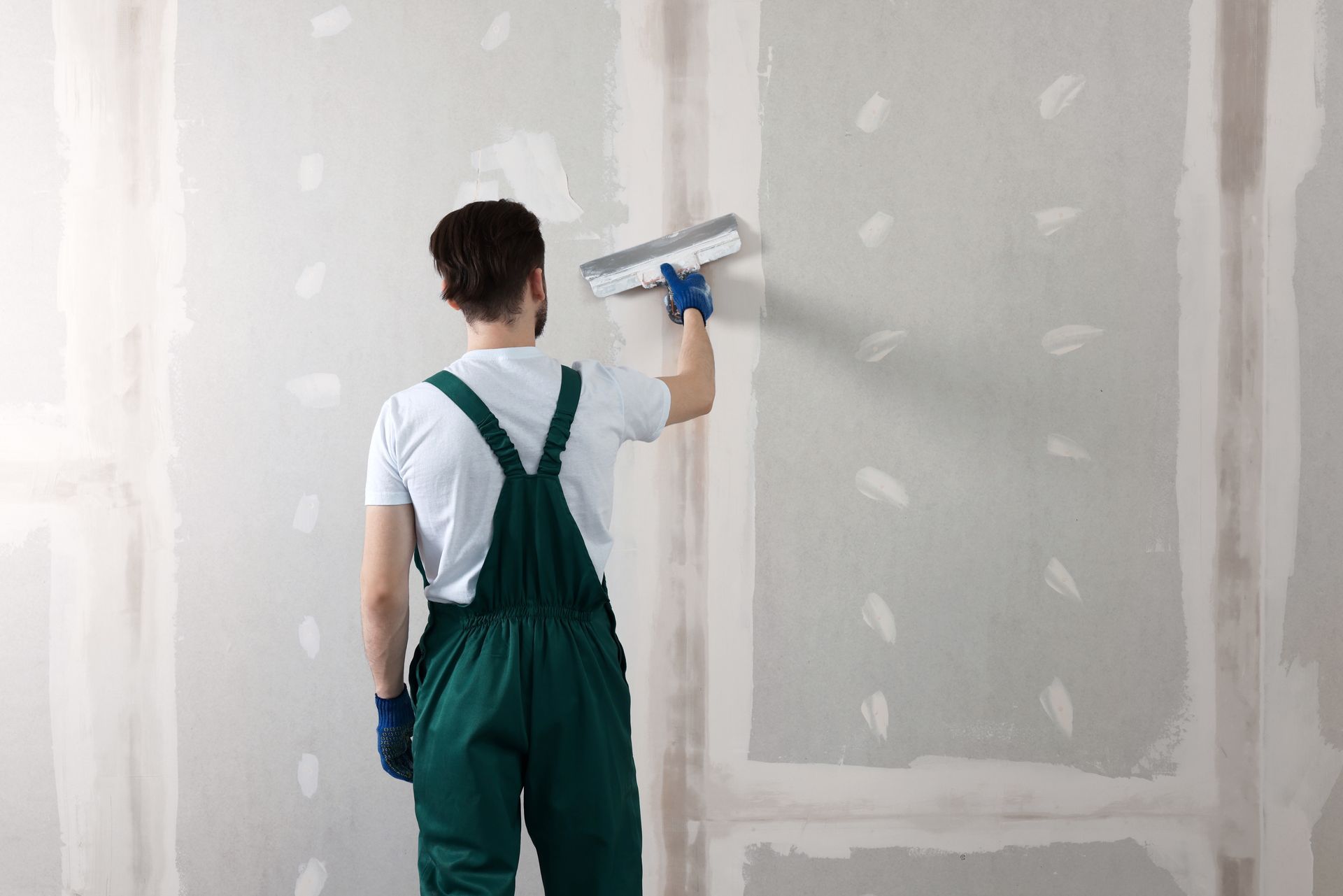 Worker smoothing drywall joints with a large taping knife on a wall.