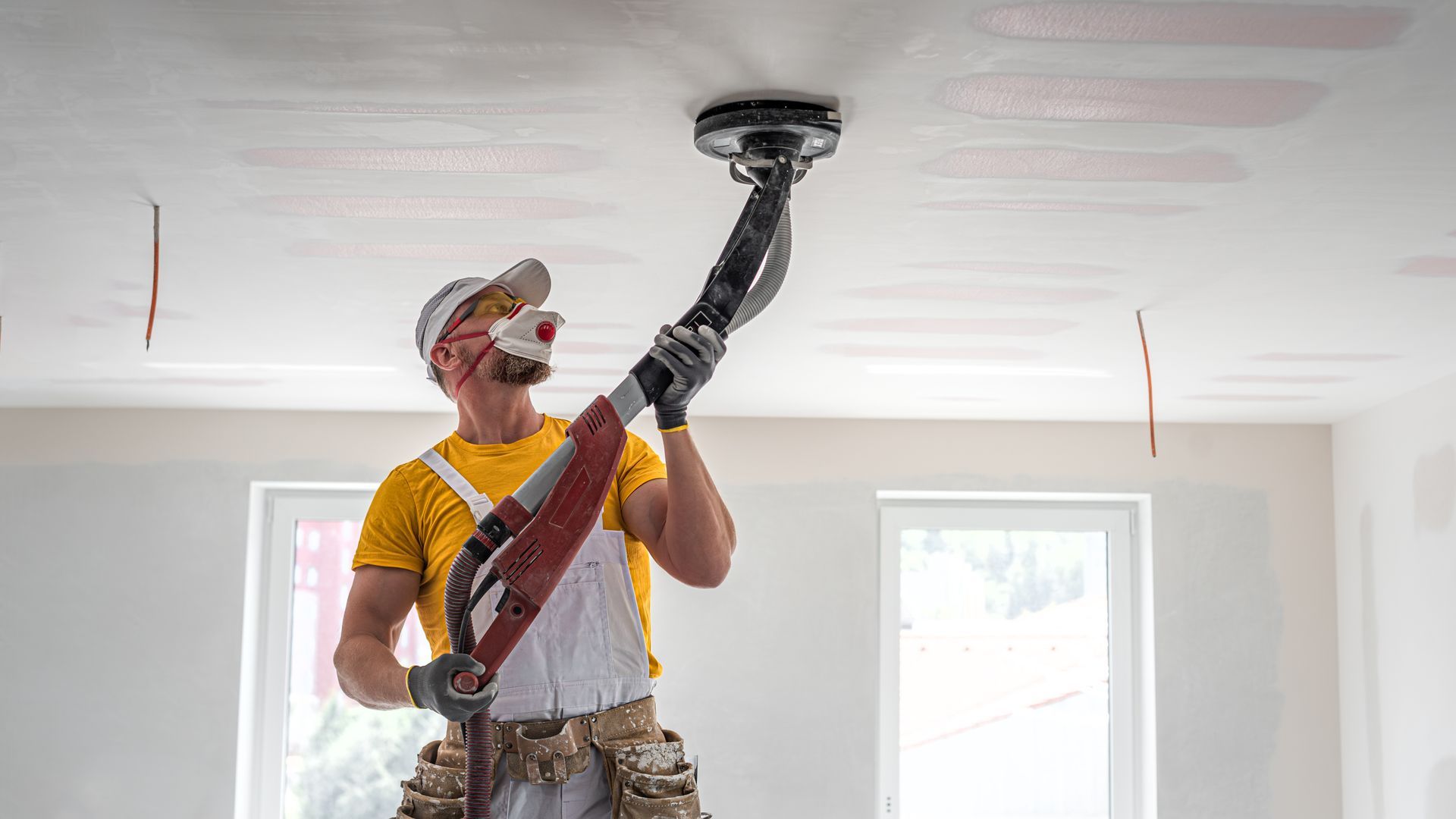 A contractor sanding a drywall ceiling using a long-reach sander.