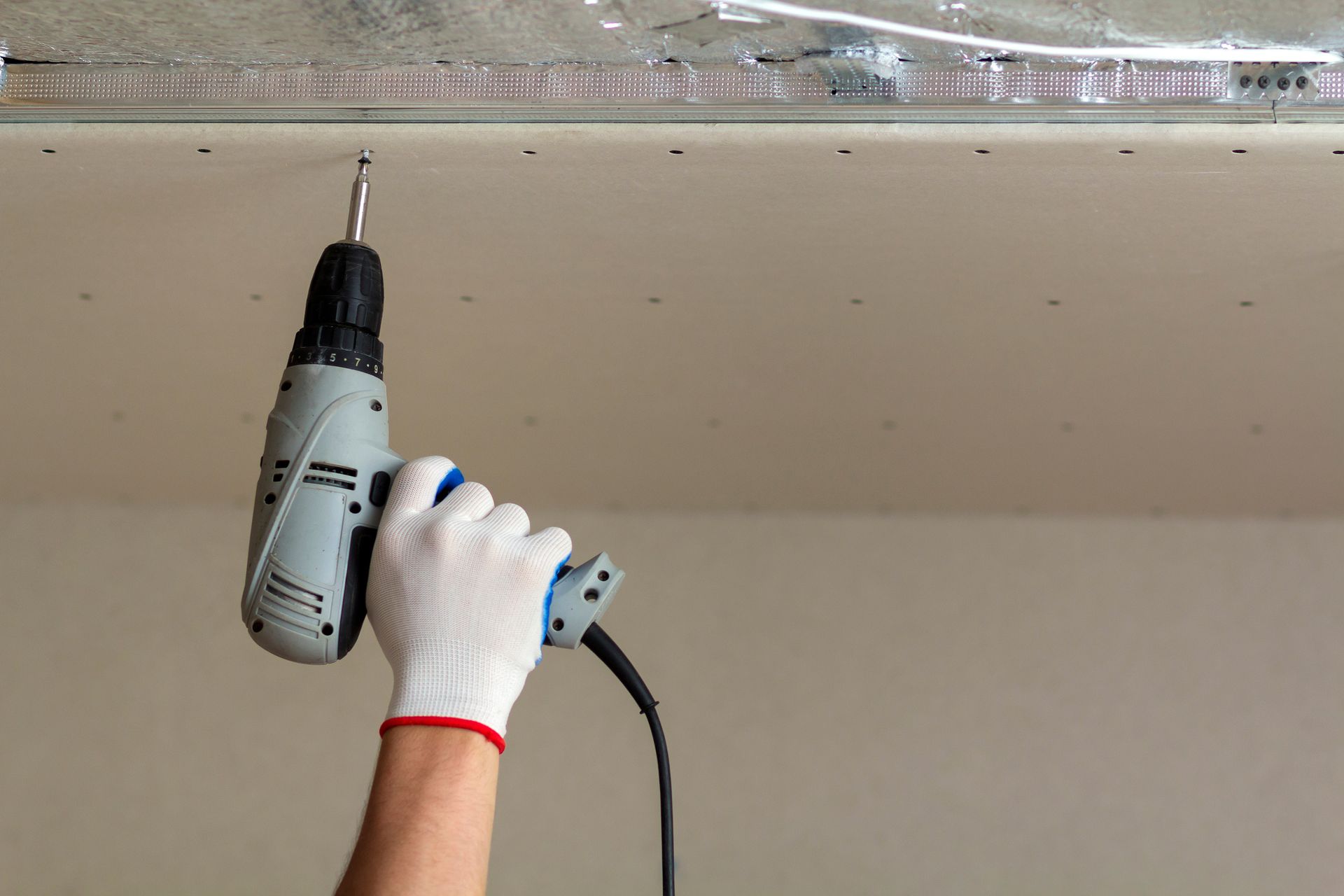 Person wearing work gloves uses a power drill to attach something to a wall.