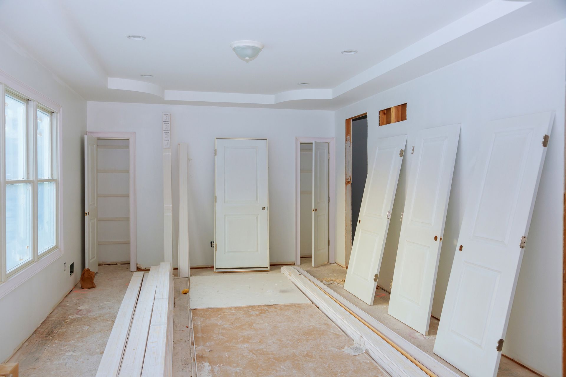 Room under renovation, white walls, doors, trim. Bare floor, empty closets.