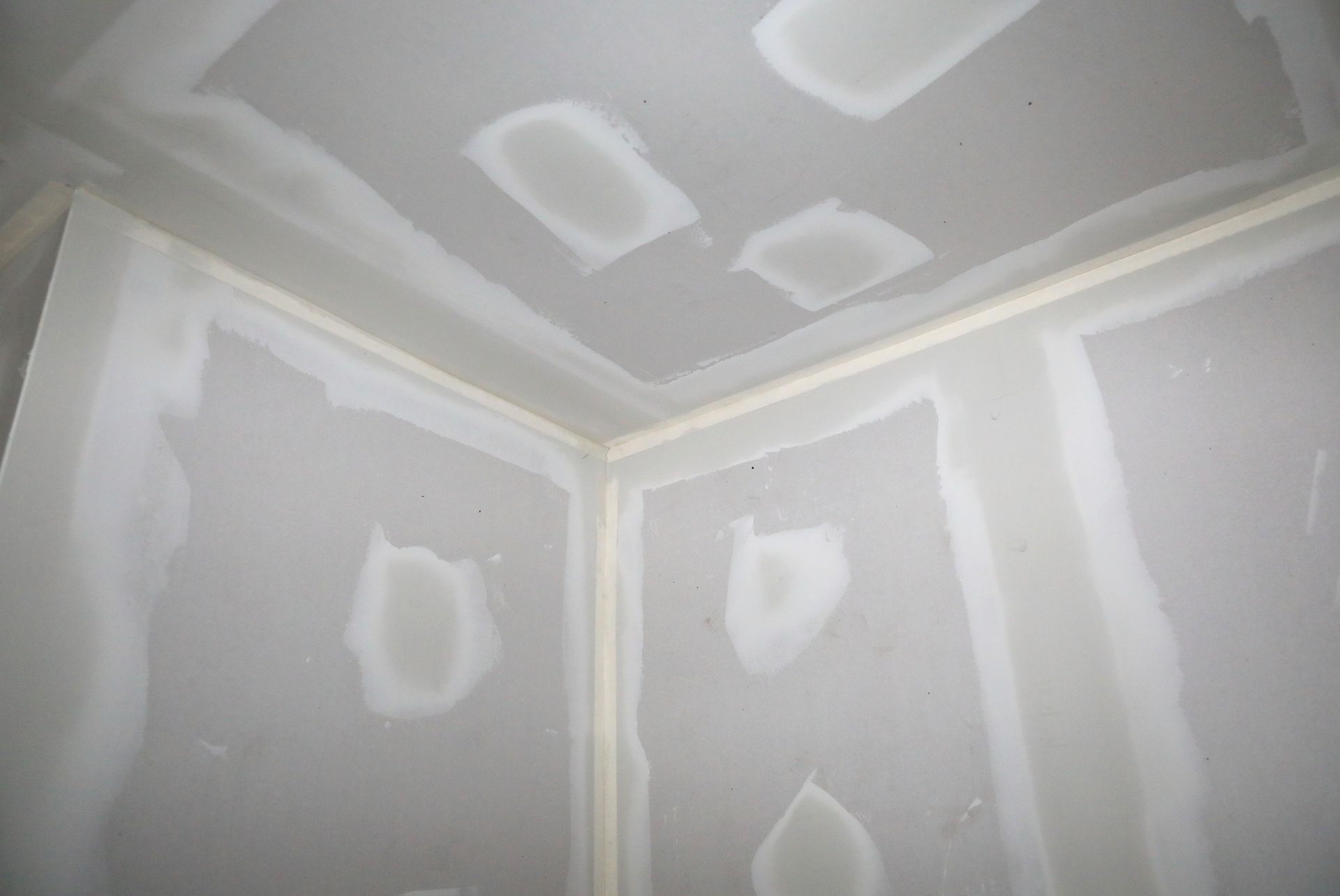 Corner of room with drywall, taped seams, and patched areas ready for finishing.