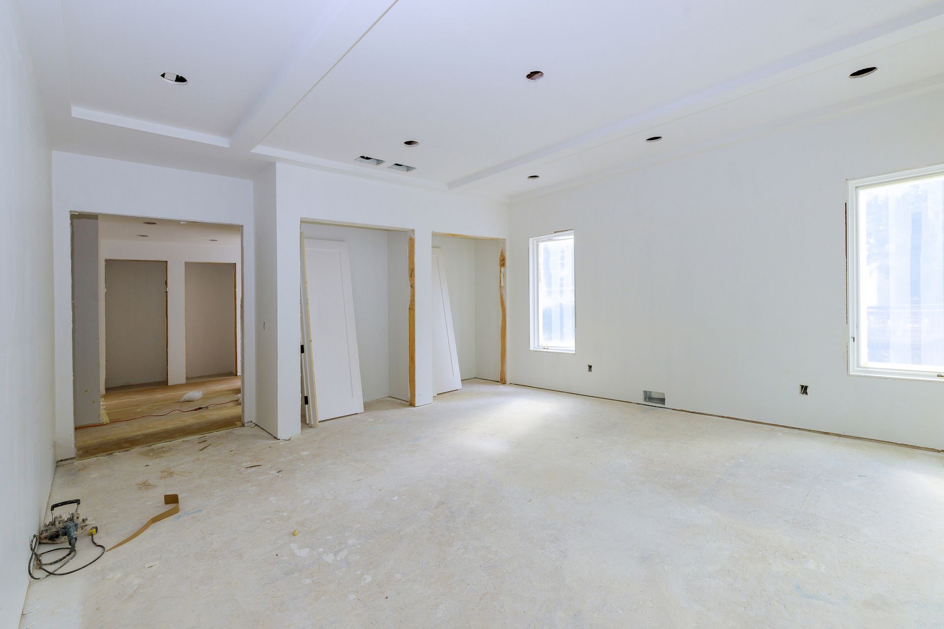 Interior of a room under construction: white walls, unfinished floor, recessed lighting, and doorways. Interior of a room under construction: white walls, unfinished floor, recessed lighting, and doorways.