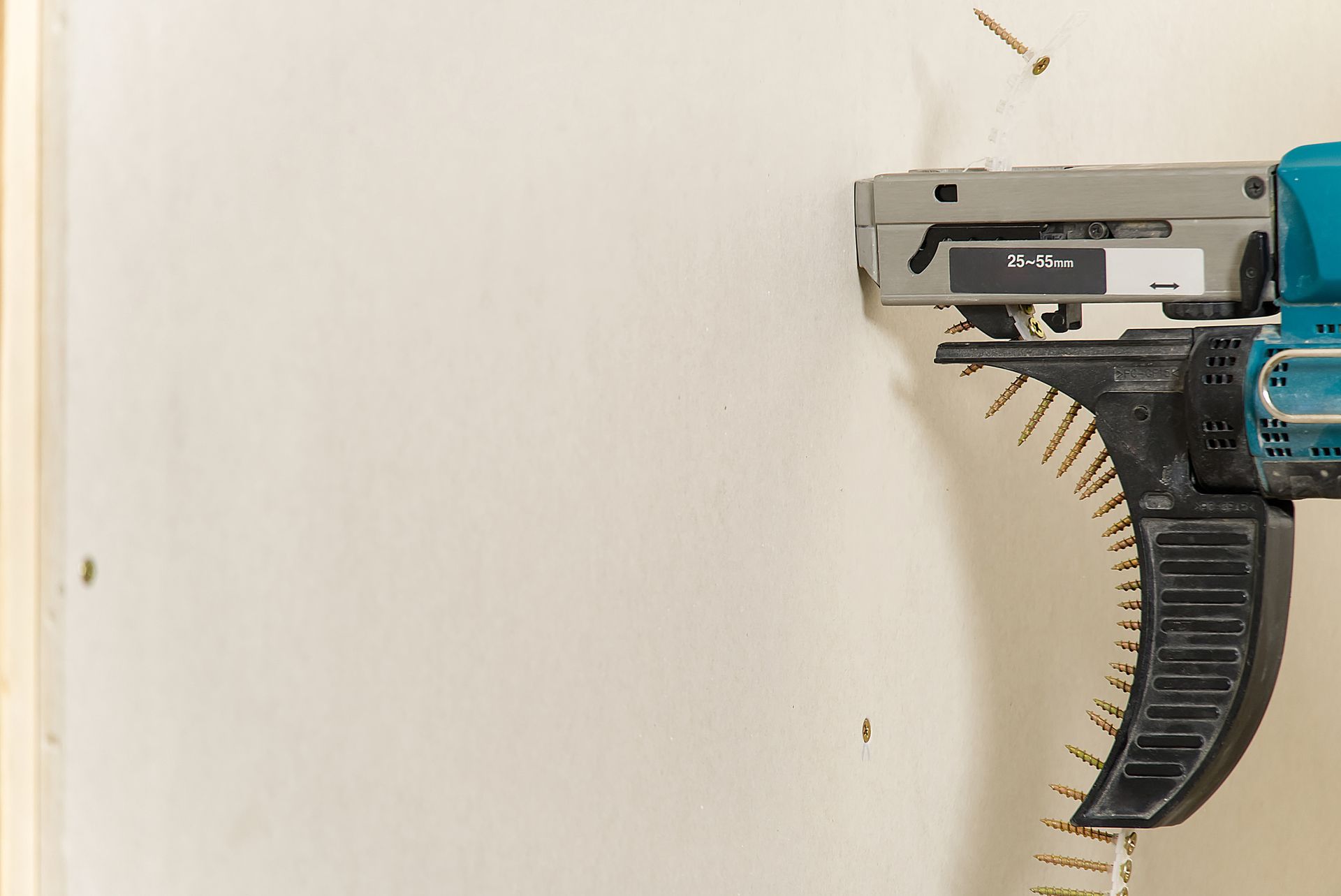 A power tool with a screw strip is drilling into a white wall, close-up. A power tool with a screw strip is drilling into a white wall, close-up.