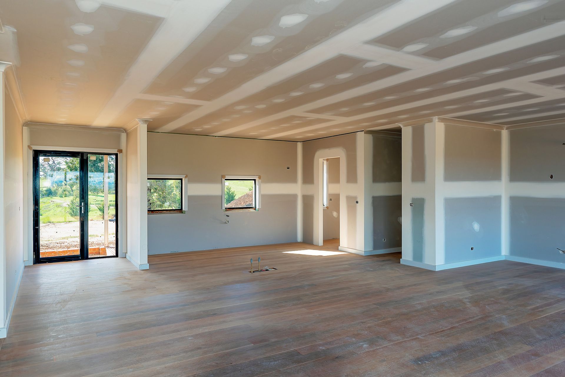 Interior of a room under construction, with drywall on walls and ceiling, and a wooden floor.