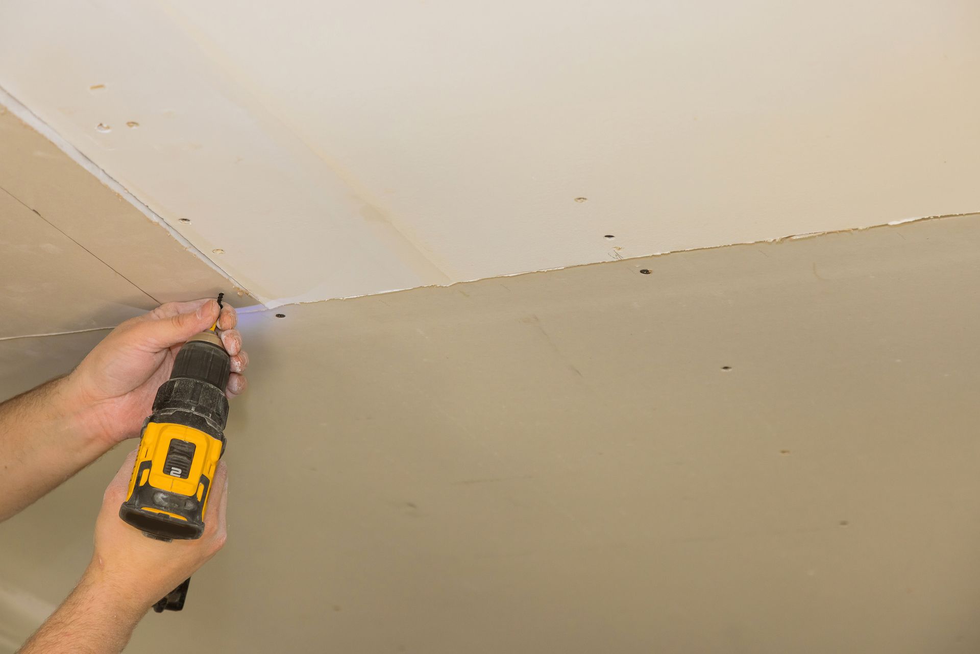 Person using a drill to screw a fastener into a ceiling. Person using a drill to screw a fastener into a ceiling.