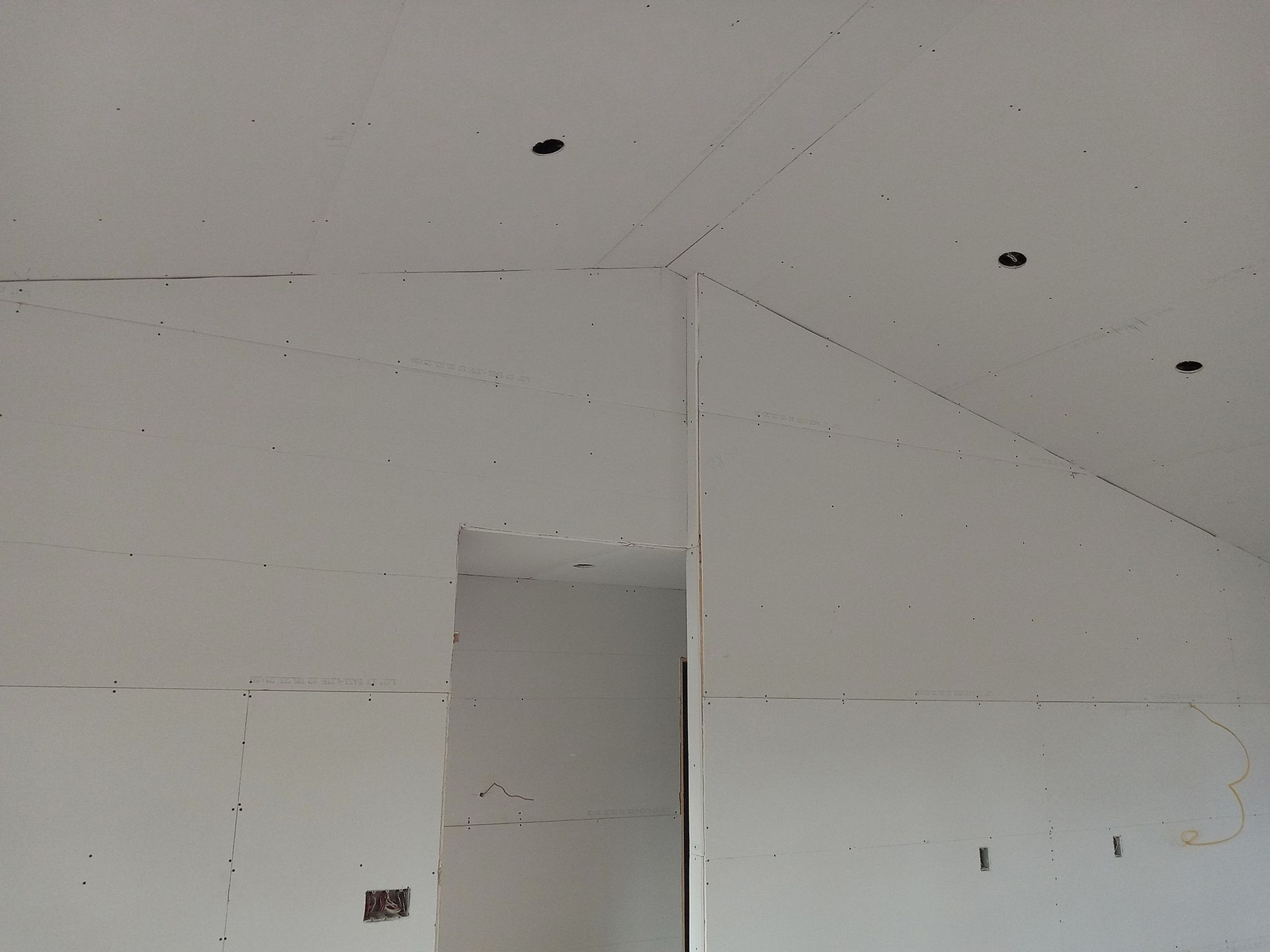 Interior view of a room with exposed drywall. The ceiling has a slanted section. There is an open doorway. Interior view of a room with exposed drywall. The ceiling has a slanted section. There is an open doorway.
