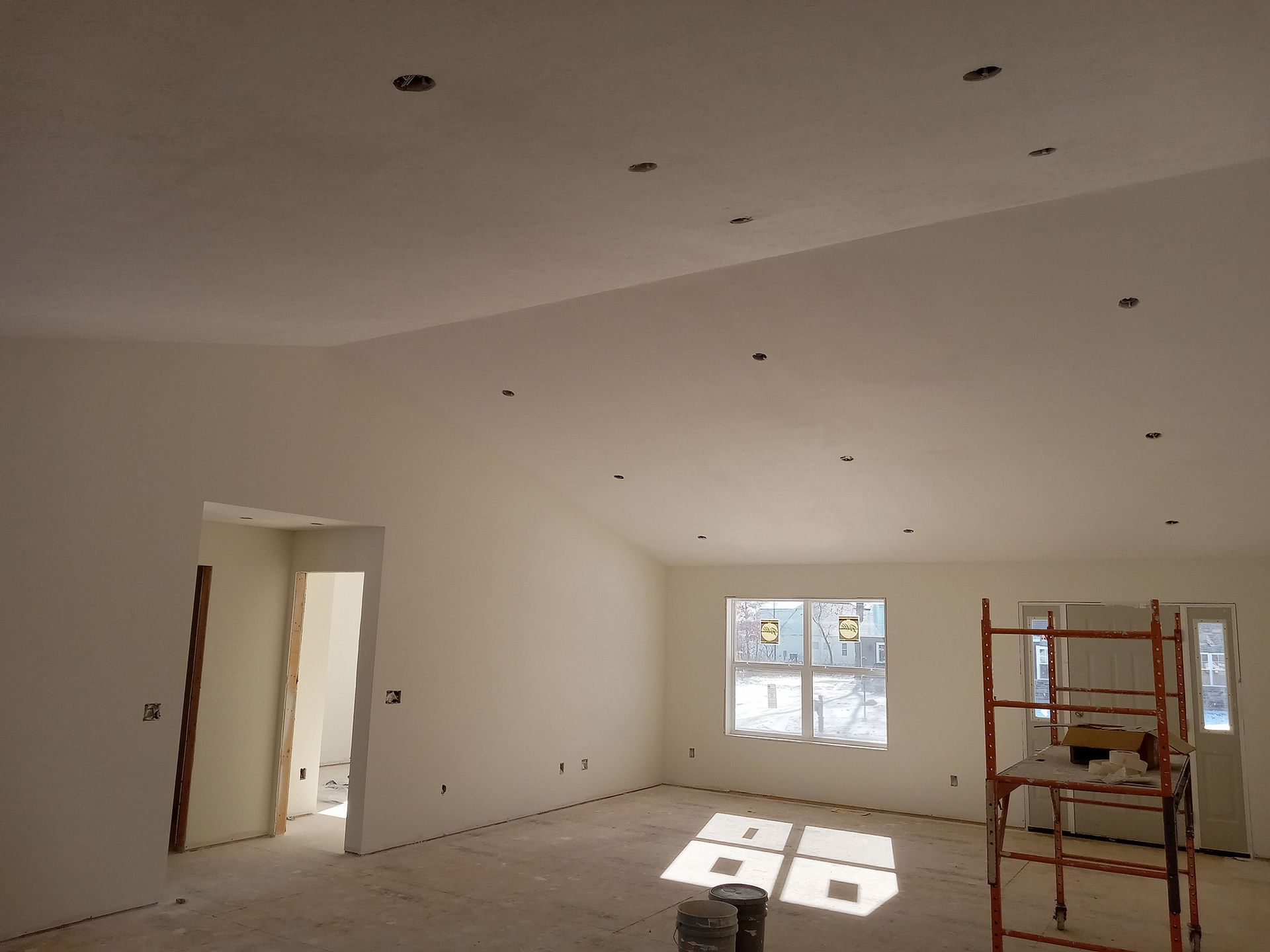 Interior of a house under construction. White walls, recessed lighting holes in the ceiling. Scaffold and window visible. Interior of a house under construction. White walls, recessed lighting holes in the ceiling. Scaffold and window visible.