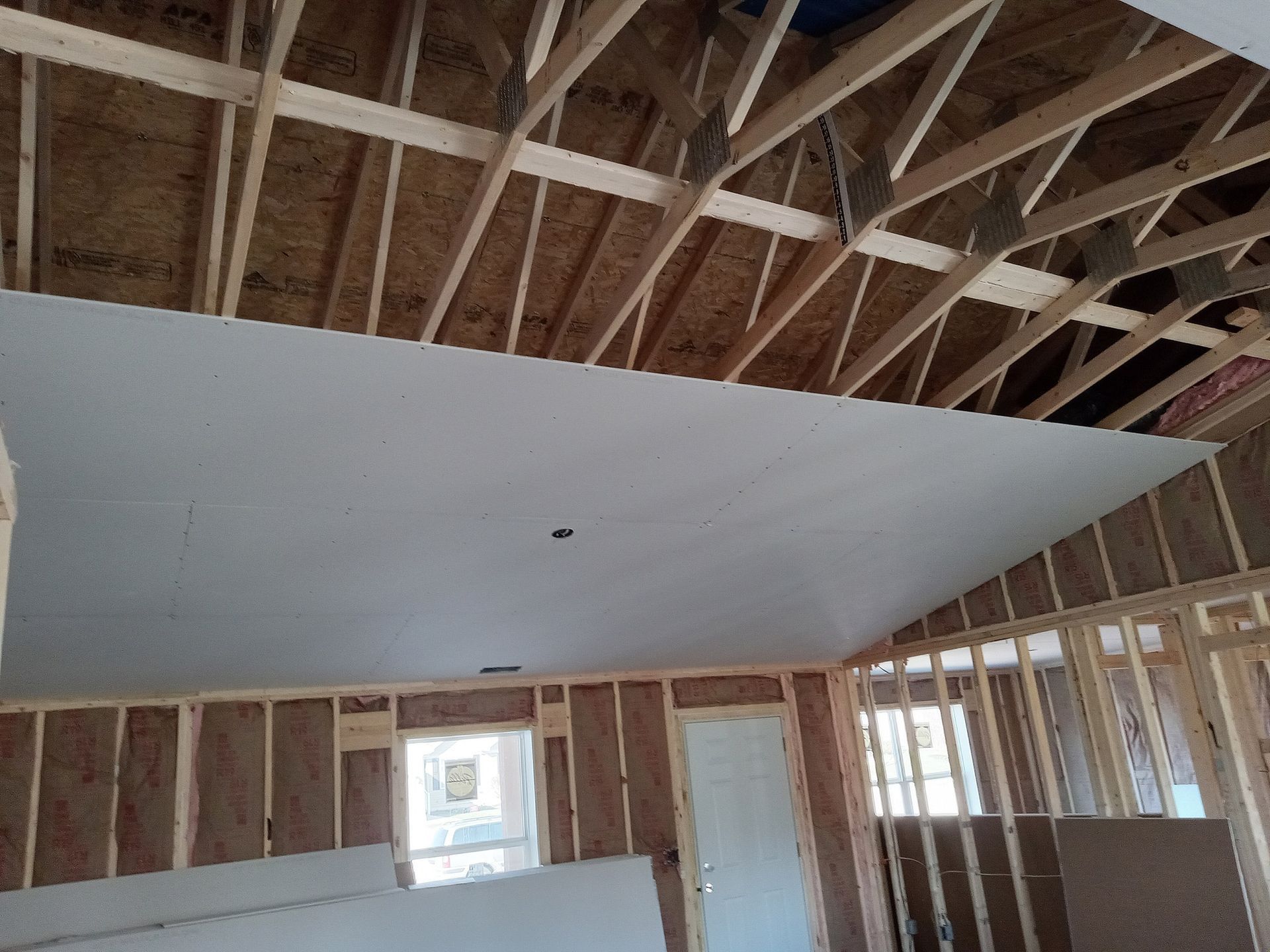 Interior of a house under construction with exposed wooden framing and drywall partially installed on the ceiling. Interior of a house under construction with exposed wooden framing and drywall partially installed on the ceiling.