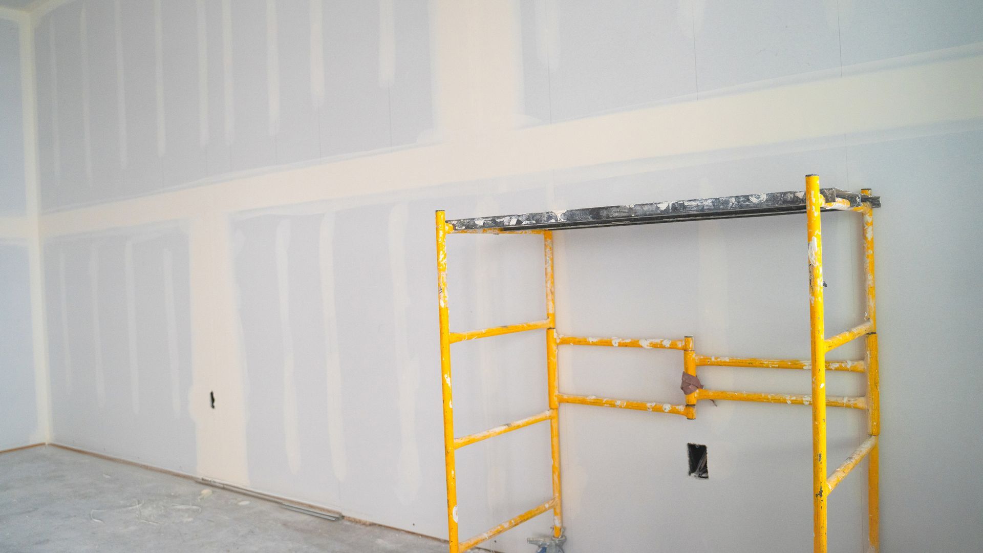 Room with drywall, partially mudded; yellow scaffold. Room with drywall, partially mudded; yellow scaffold.