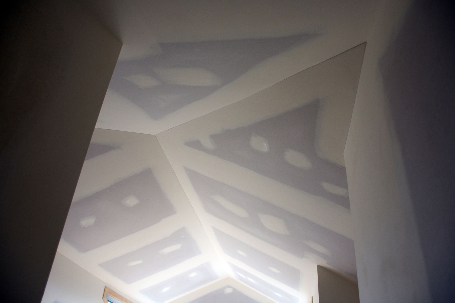 Angled ceiling with drywall, patches and a light color.