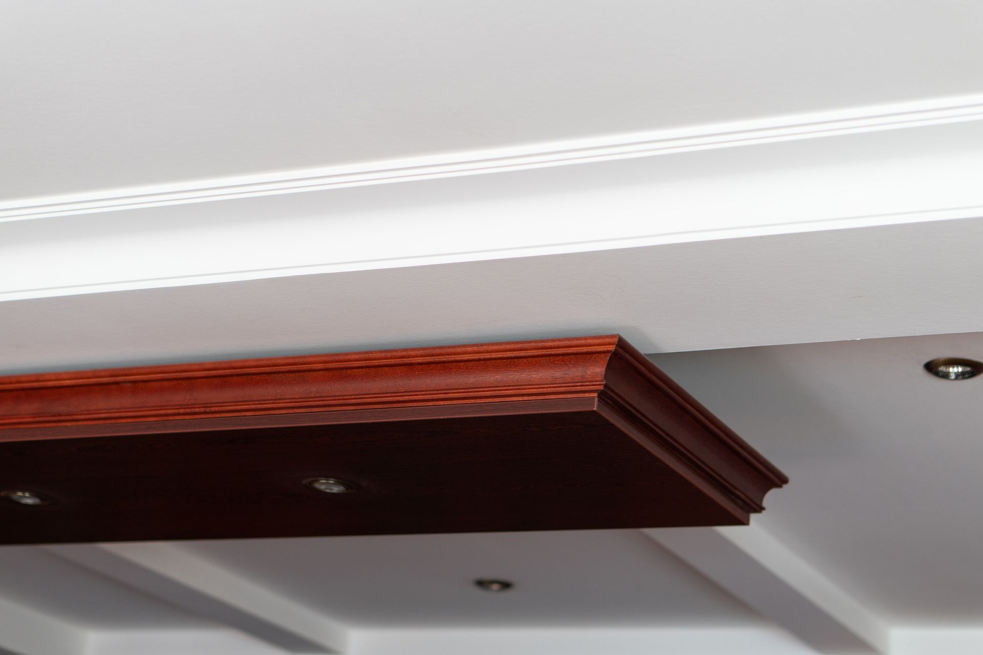 Close-up of a ceiling with a dark wood panel and a white, decorative crown molding. Close-up of a ceiling with a dark wood panel and a white, decorative crown molding.
