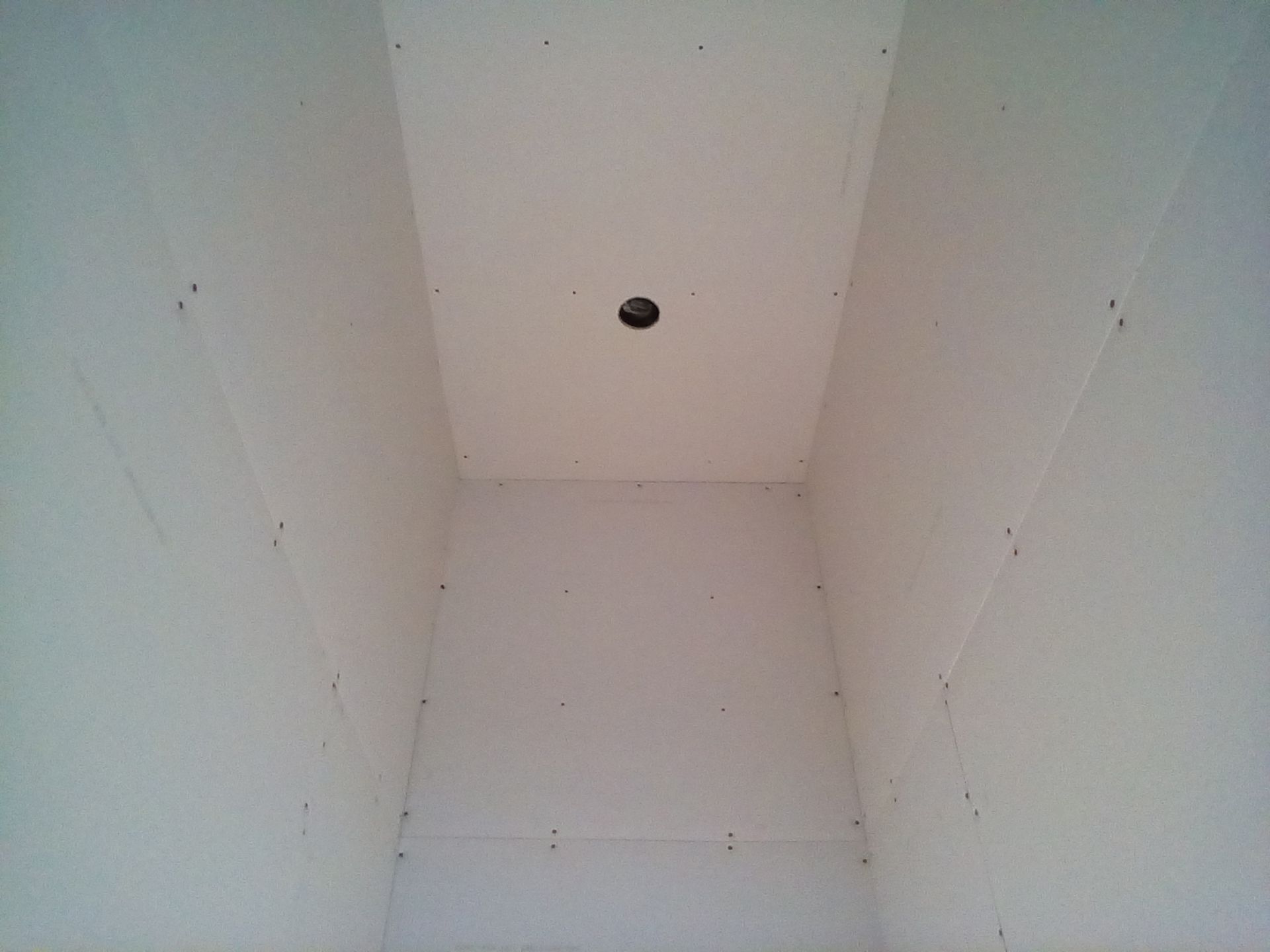 Interior of a small room with white drywall walls and a ceiling, a hole for a light fixture. Interior of a small room with white drywall walls and a ceiling, a hole for a light fixture.