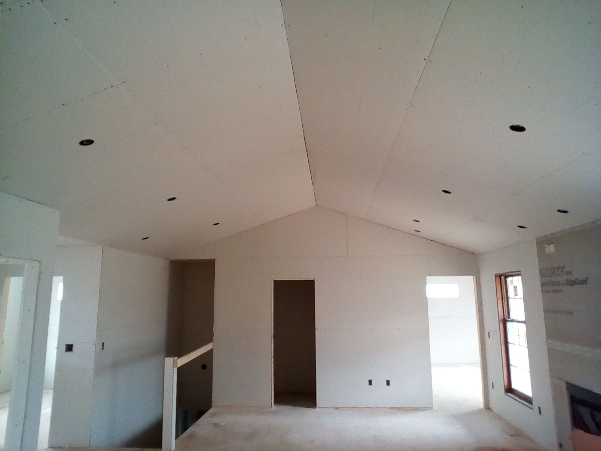 Interior of a house under construction with drywall on walls and ceiling, open doorways, and recessed lighting. Interior of a house under construction with drywall on walls and ceiling, open doorways, and recessed lighting.