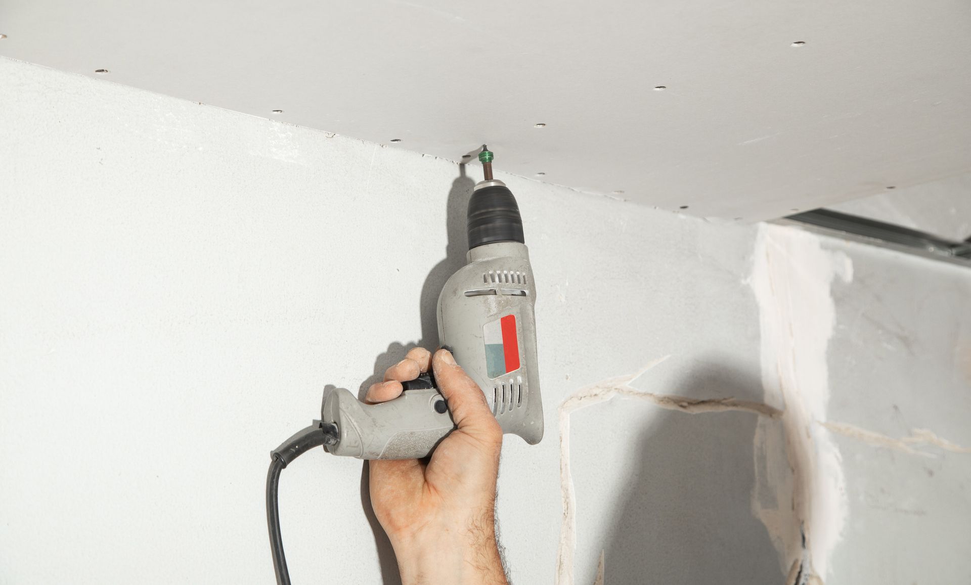 Hand using a power drill to screw into a white ceiling. Hand using a power drill to screw into a white ceiling.