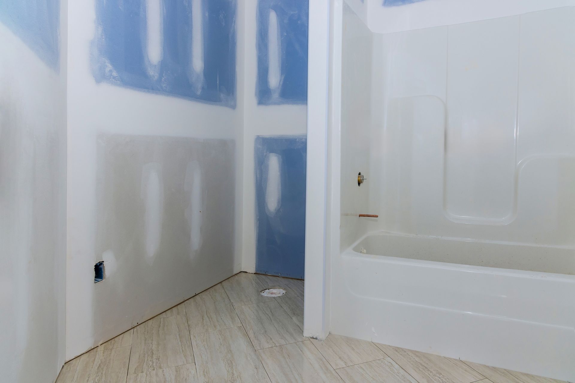 Bathroom under construction; drywall, shower/tub unit, and light-colored flooring visible. Bathroom under construction; drywall, shower/tub unit, and light-colored flooring visible.