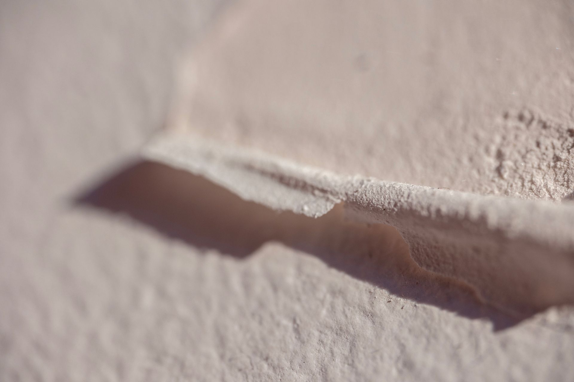 Close-up of a light-colored wall with a crevice casting a shadow. Close-up of a light-colored wall with a crevice casting a shadow.