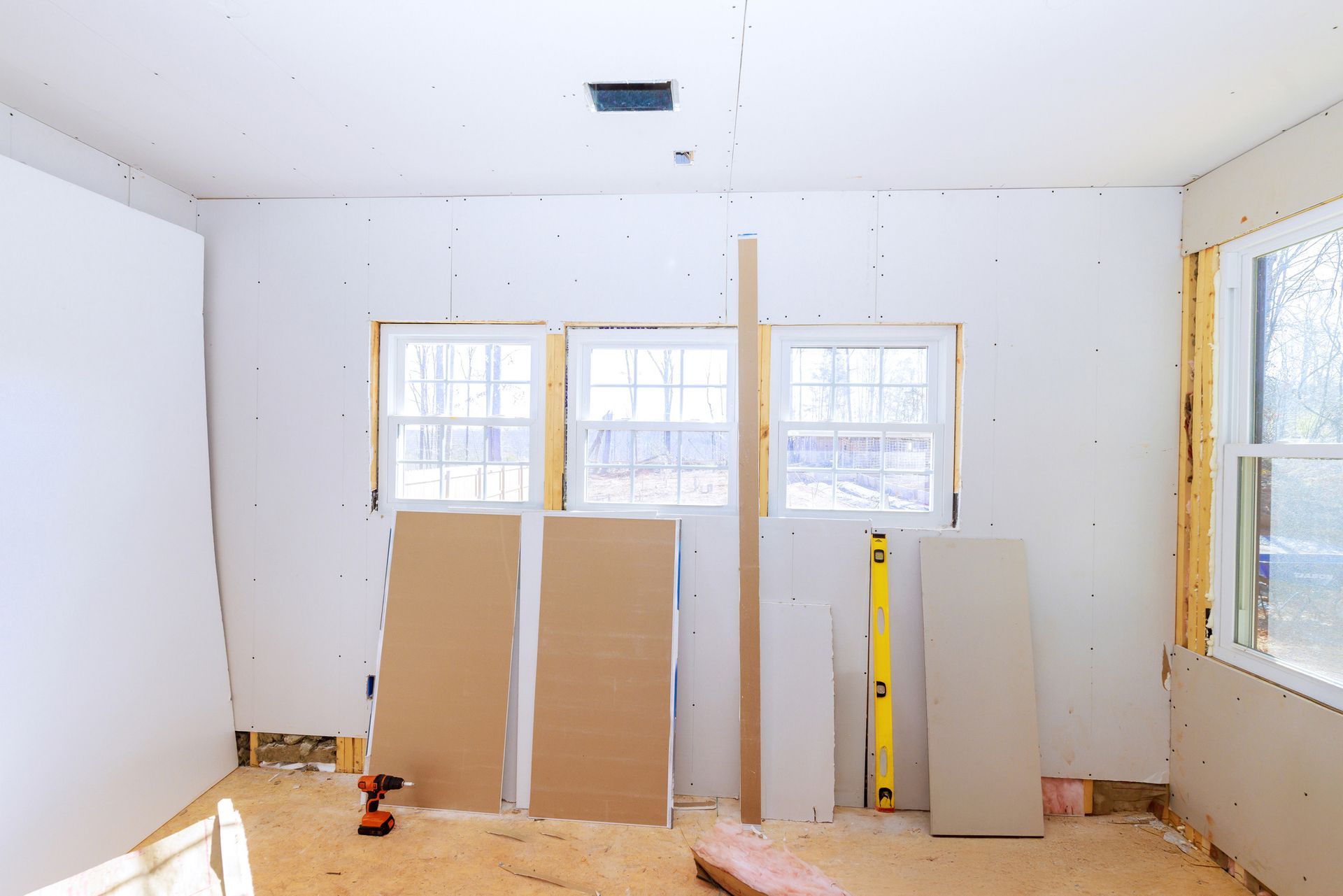 Room renovation in progress with drywall, windows, and tools scattered about. Room renovation in progress with drywall, windows, and tools scattered about.
