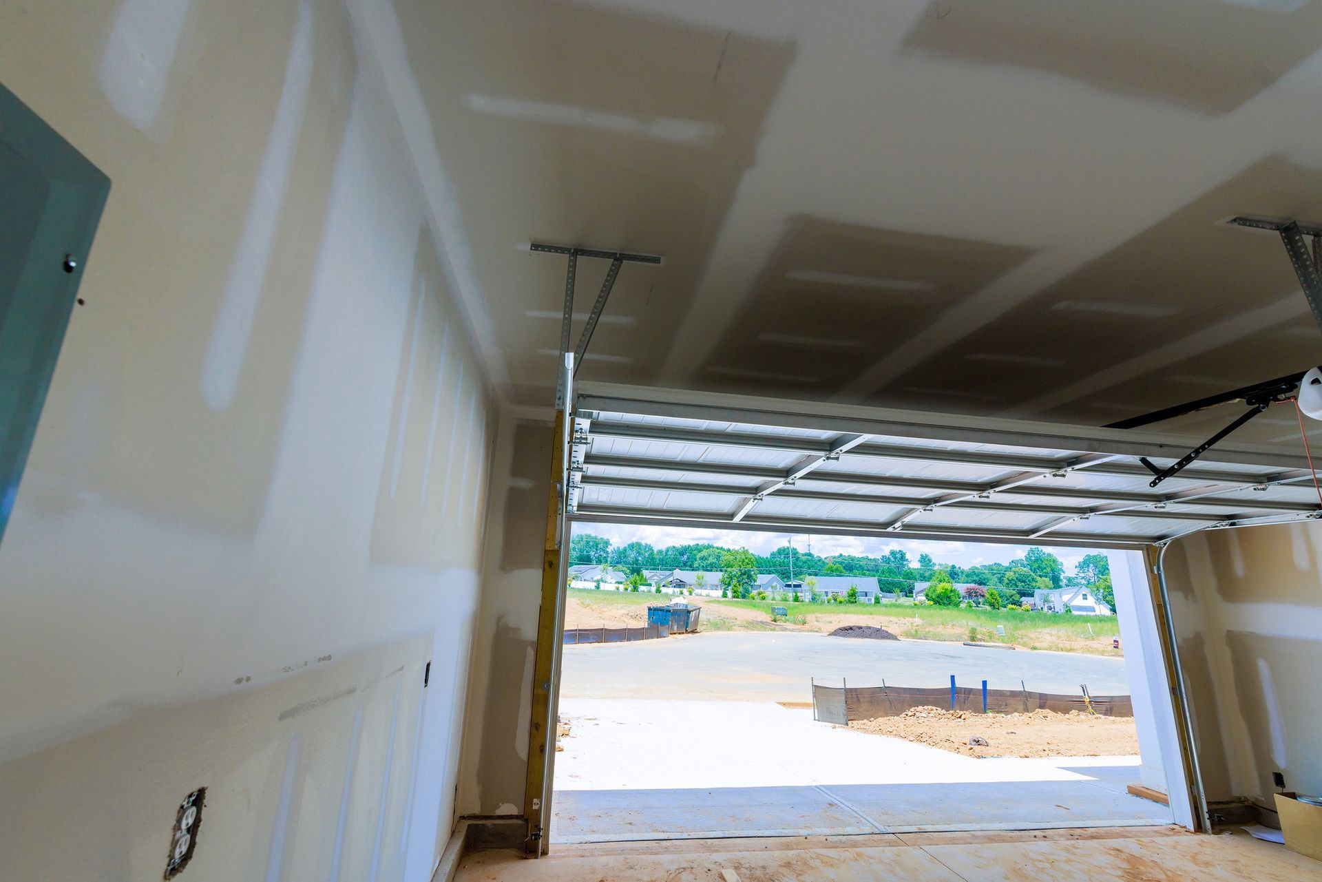 Interior of a garage under construction with drywall on walls and ceiling, opening to outdoor view. Interior of a garage under construction with drywall on walls and ceiling, opening to outdoor view.