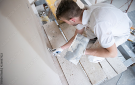 Person applying plaster to a wall with a trowel, working indoors. Person applying plaster to a wall with a trowel, working indoors.