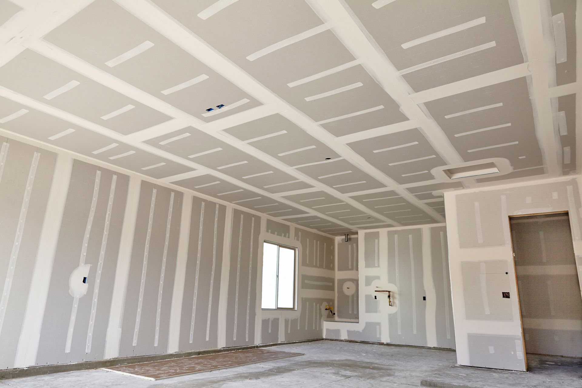 Drywall installation in a room, walls and ceiling. Gray drywall with white tape and joint compound.