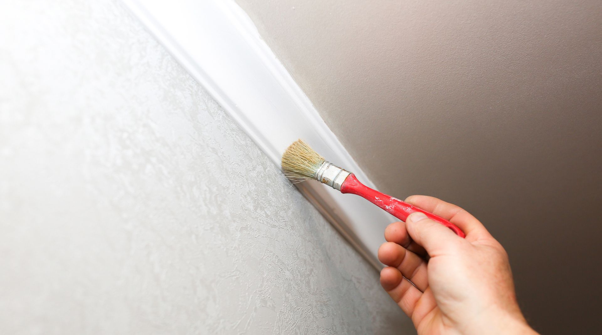 Hand painting white trim with a brush against a white textured wall and ceiling.