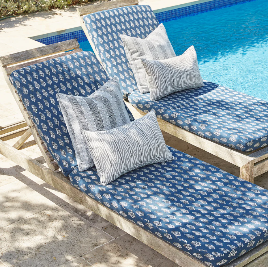 Two wooden lounge chairs with blue patterned cushions and patterned throw pillows beside a swimming pool.