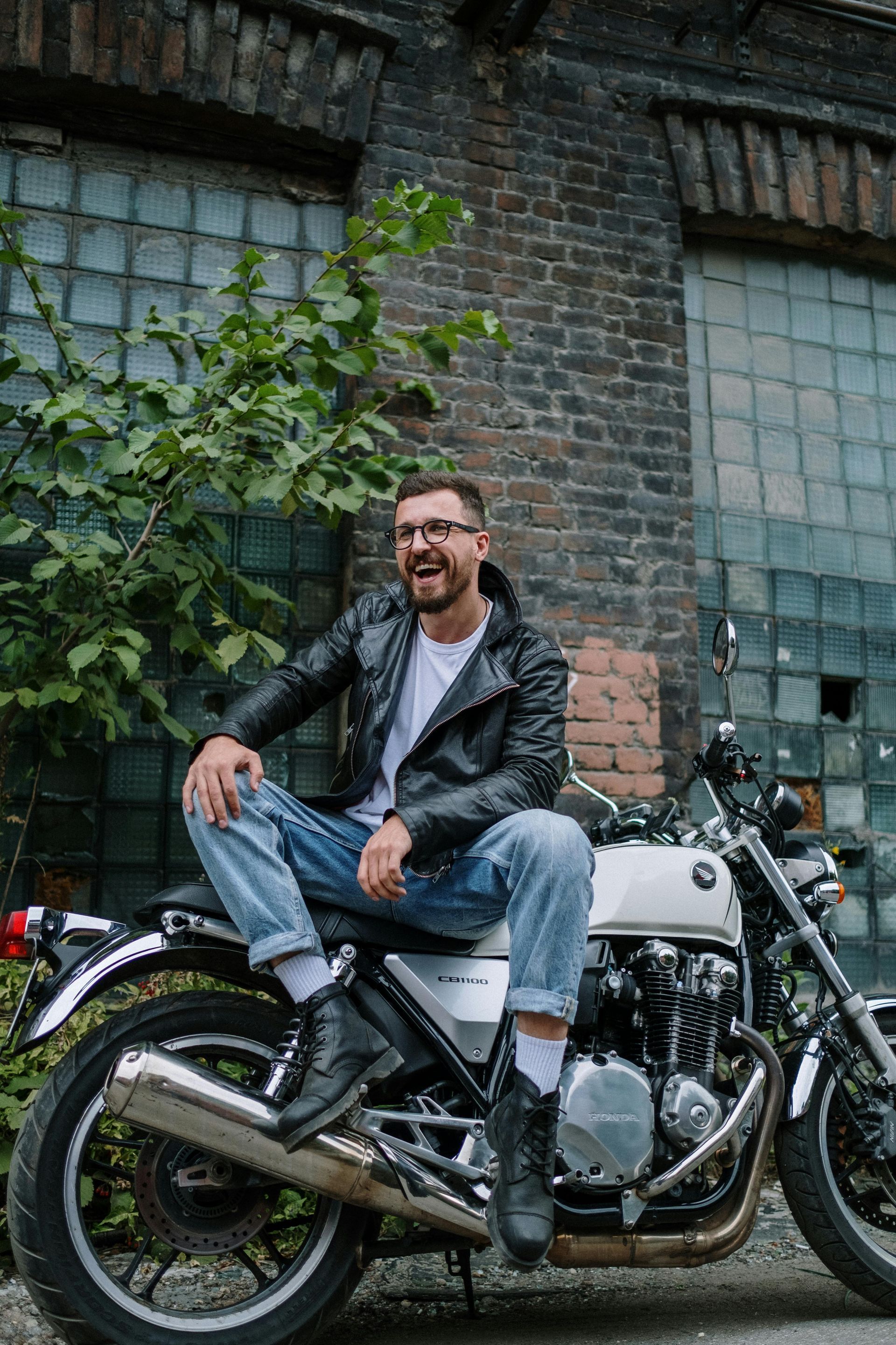 A man in a leather jacket is sitting on a motorcycle.