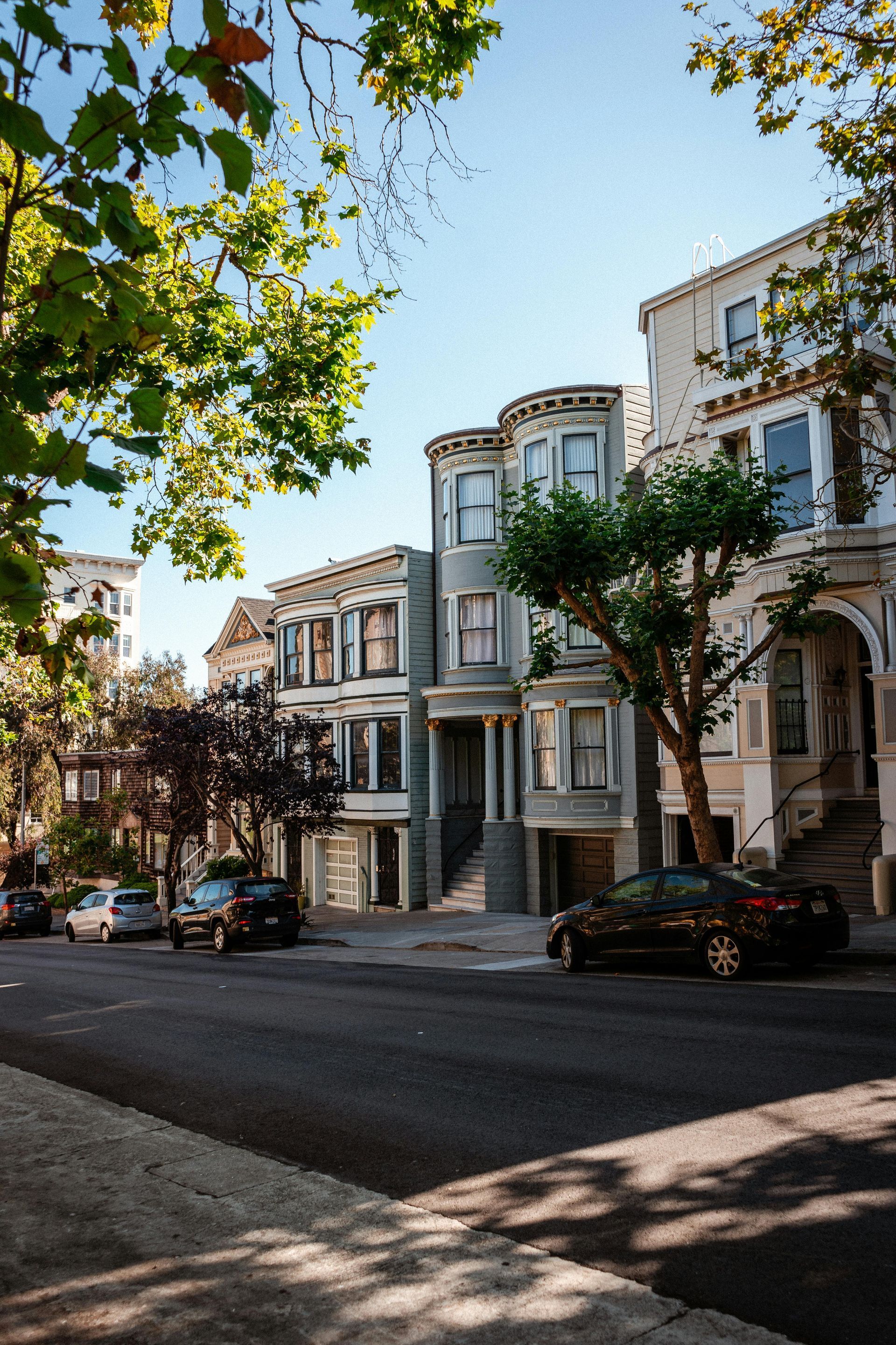 A black car is parked on the side of the road in front of a row of houses.