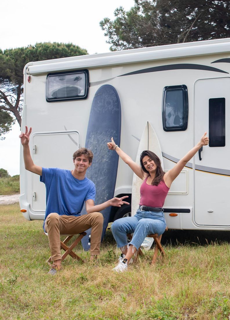 A man and a woman are sitting in front of a rv.