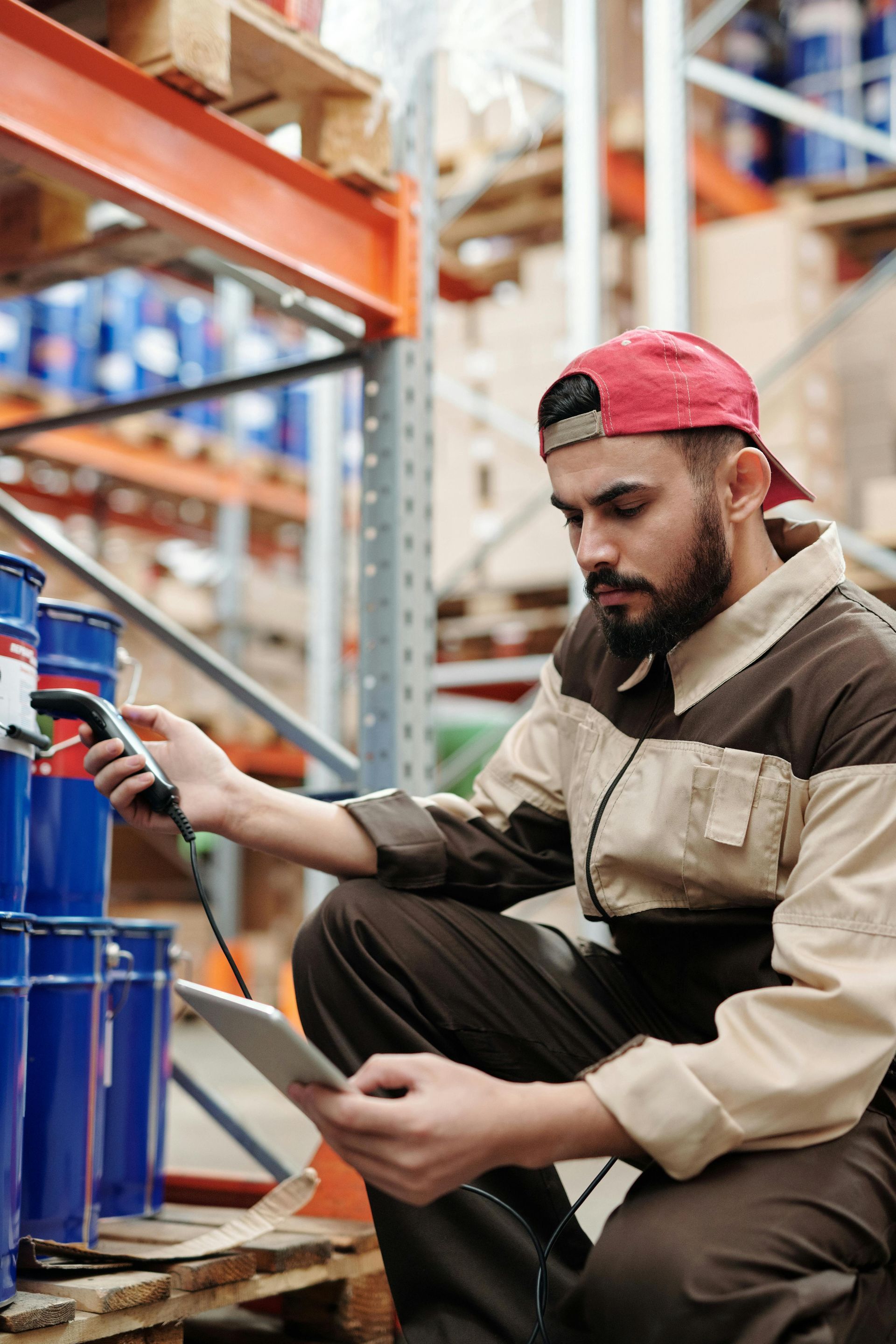 A man is kneeling down in a warehouse using a scanner and a tablet.