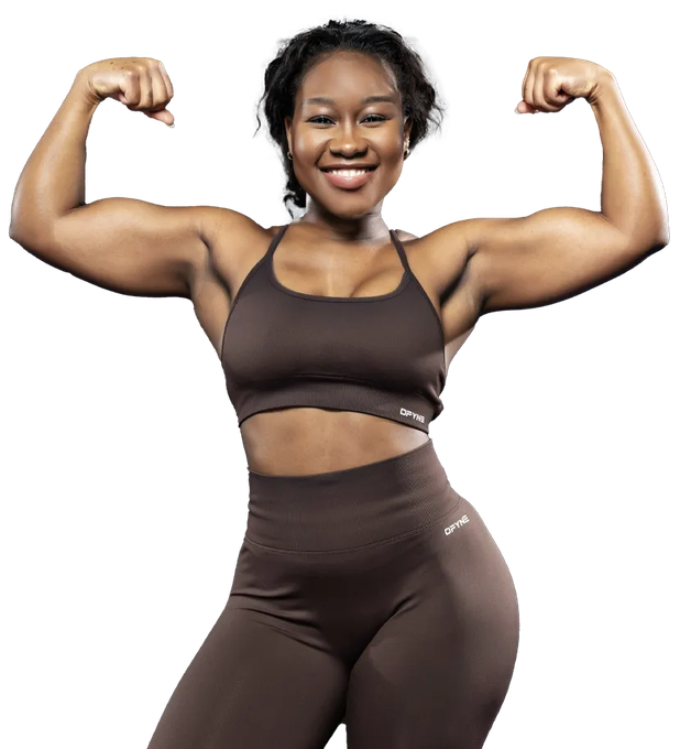 A woman in a green crop top and black shorts is smiling. Become Your Fit - Nikki