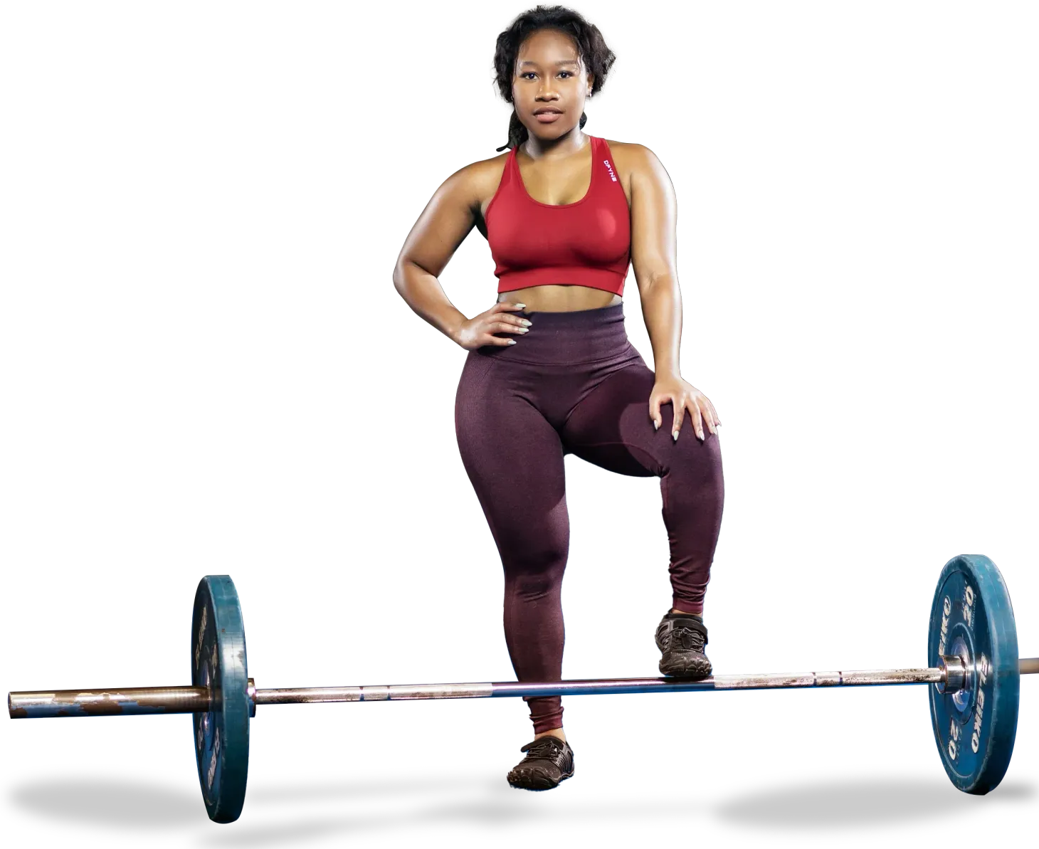 Woman in workout attire poses with barbell, one foot on it.