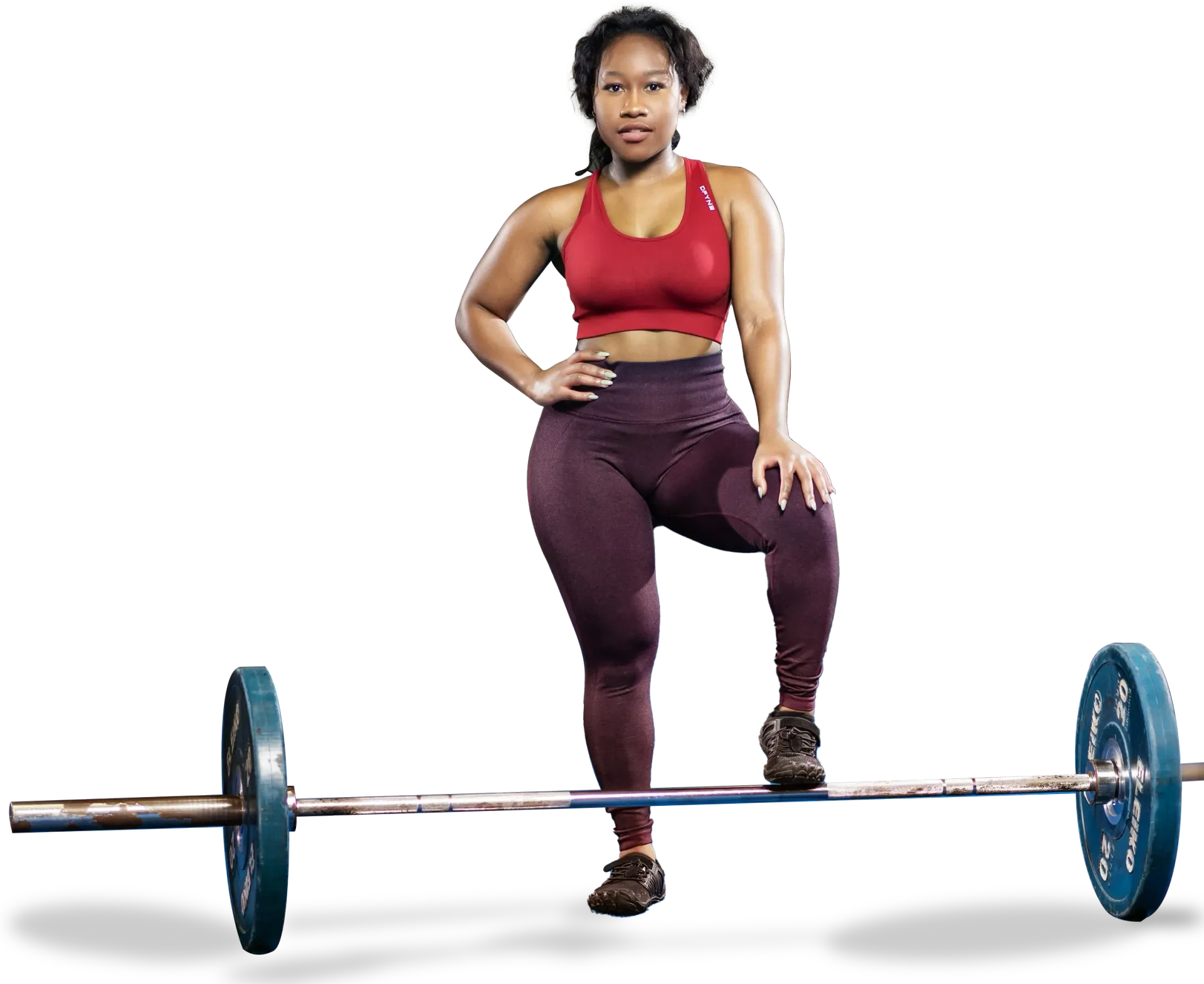 Woman in workout attire poses with barbell, one foot on it.