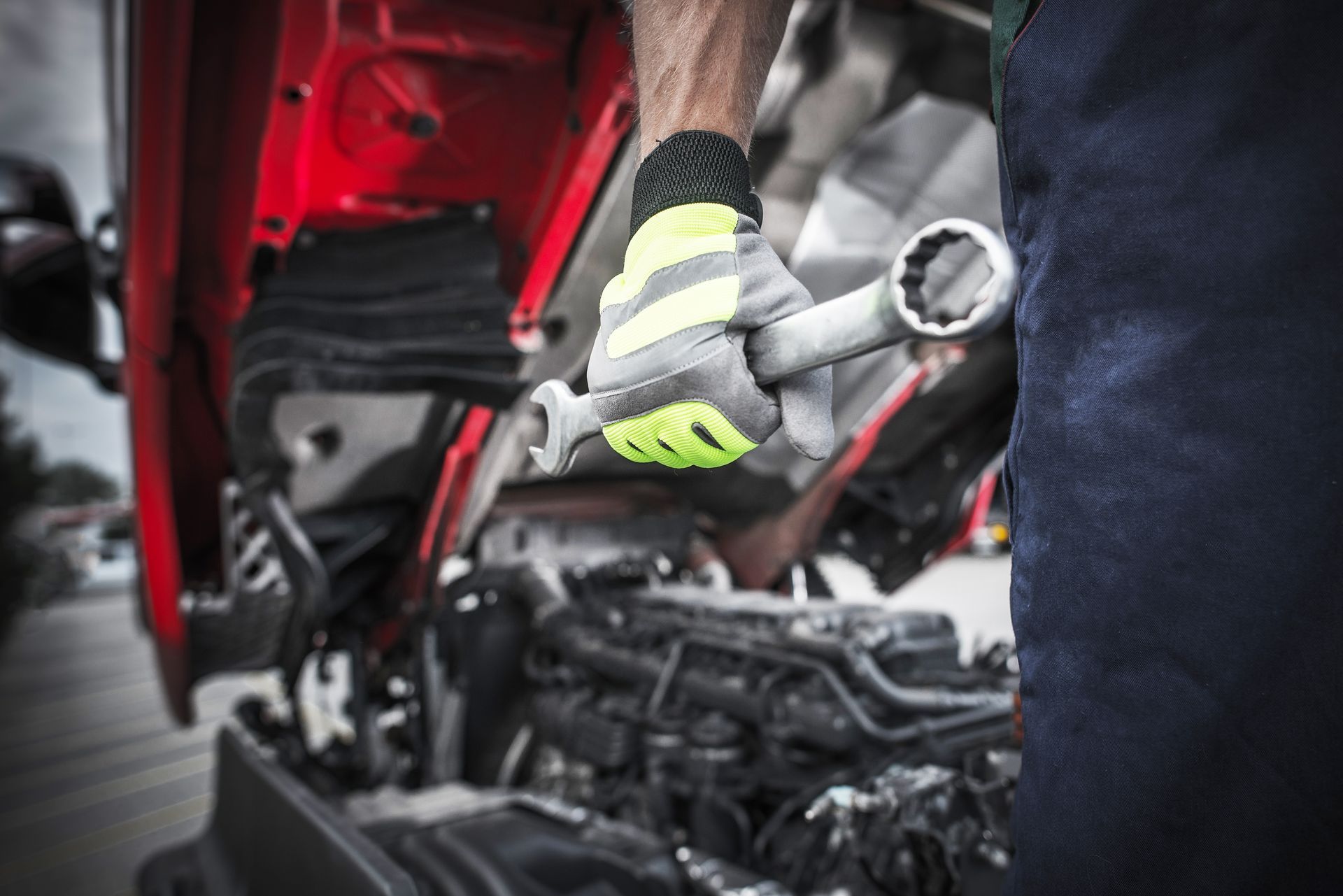 Close-up of a mechanic holding a wrench near a truck engine with hood open.