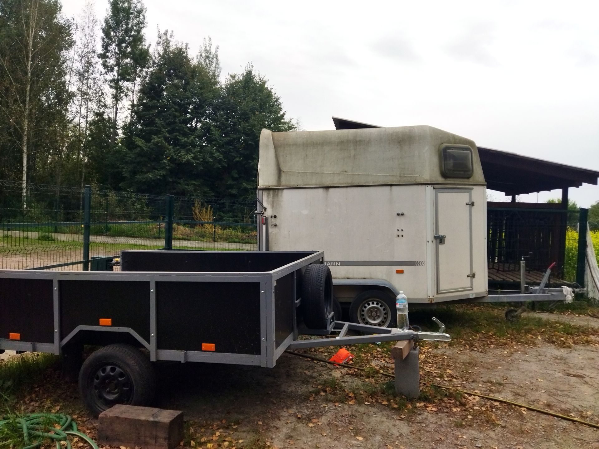 Two trailers parked outdoors near a fenced area with trees in the background.