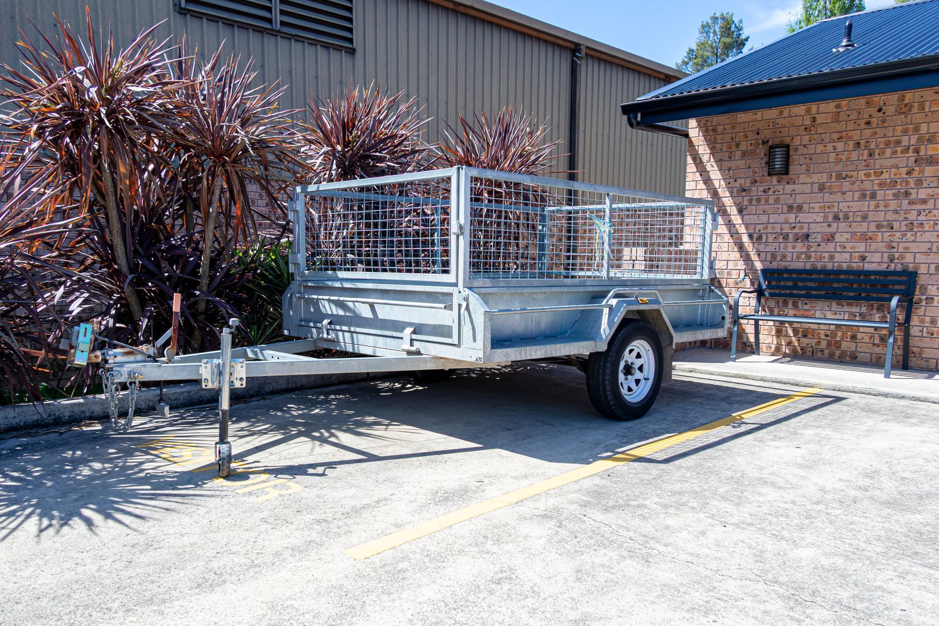 A parked galvanized single axel steel trailer with a mesh cage section.