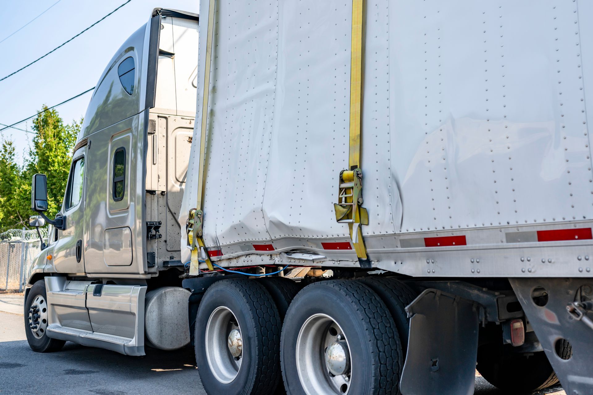 Beige semi-truck with damaged trailer secured by sling, awaiting street repair. Beige semi-truck with damaged trailer secured by sling, awaiting street repair.