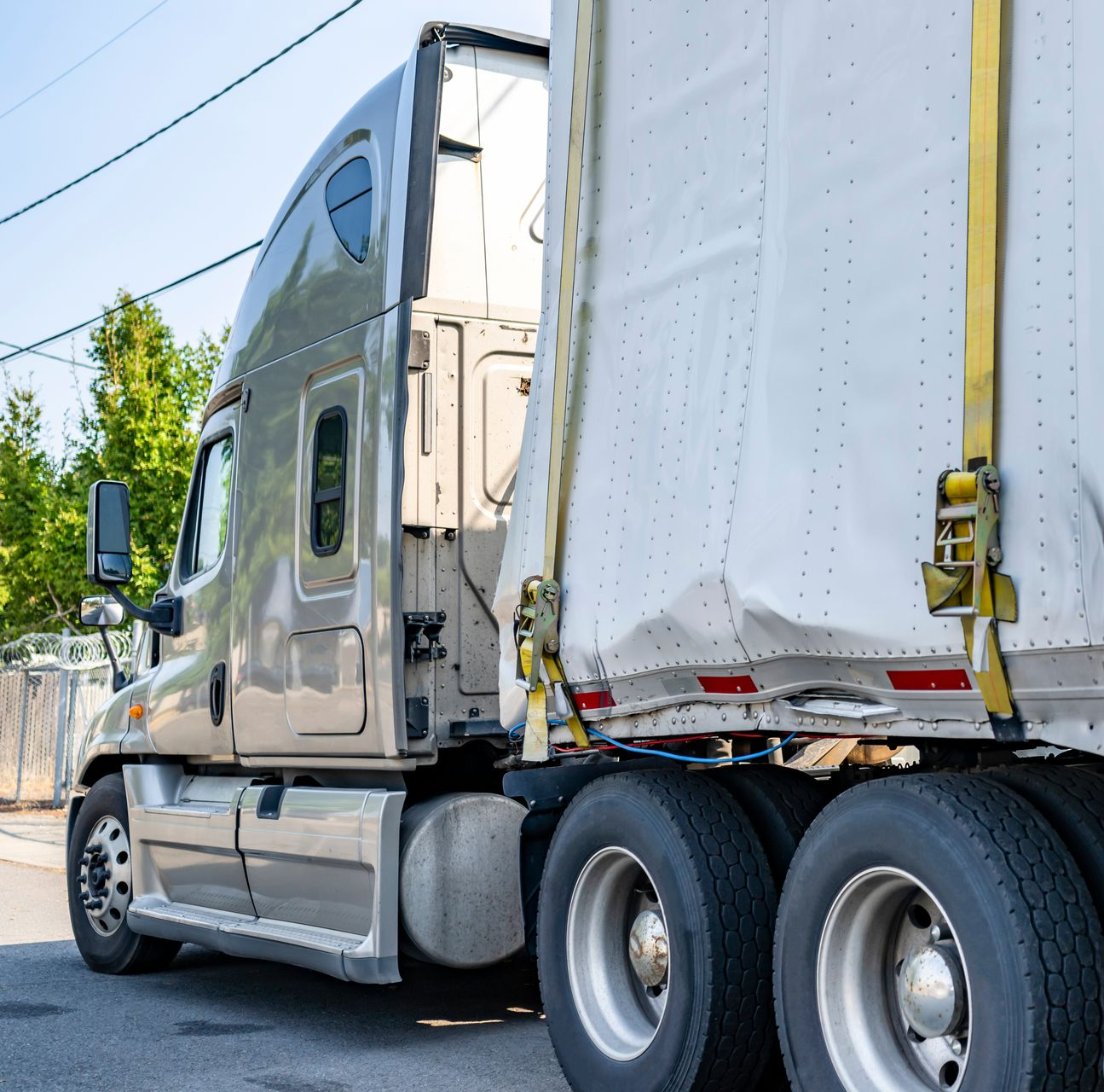 Beige semi-truck with damaged trailer secured by sling, awaiting street repair. Beige semi-truck with damaged trailer secured by sling, awaiting street repair.