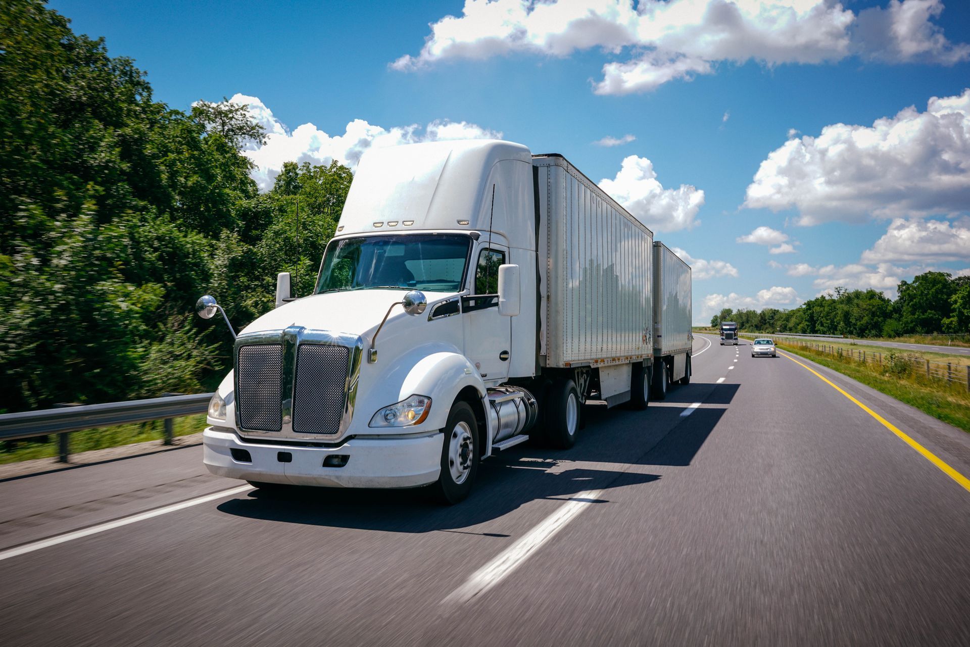 White semi truck hauling cargo trailers on highway under blue sky, long haul freight transportation.